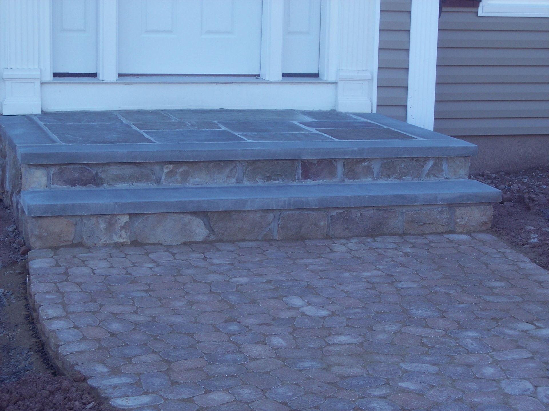 Stone front steps and a curved cobblestone walkway leading to a white house entrance
