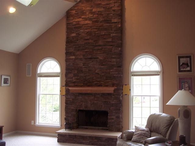 Living room with stone fireplace, two arched windows, beige walls, and a sofa with lamp
