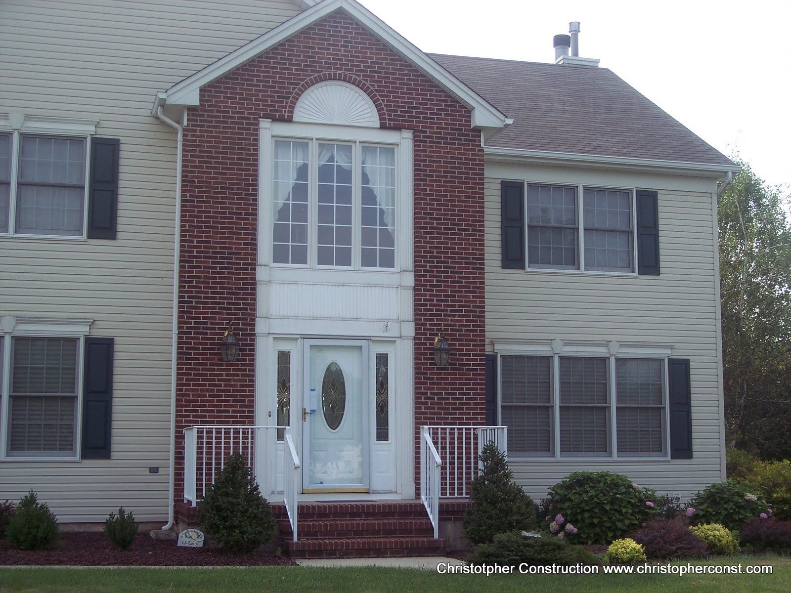 Two-story house with red brick center, light siding, black shutters, and a white front door