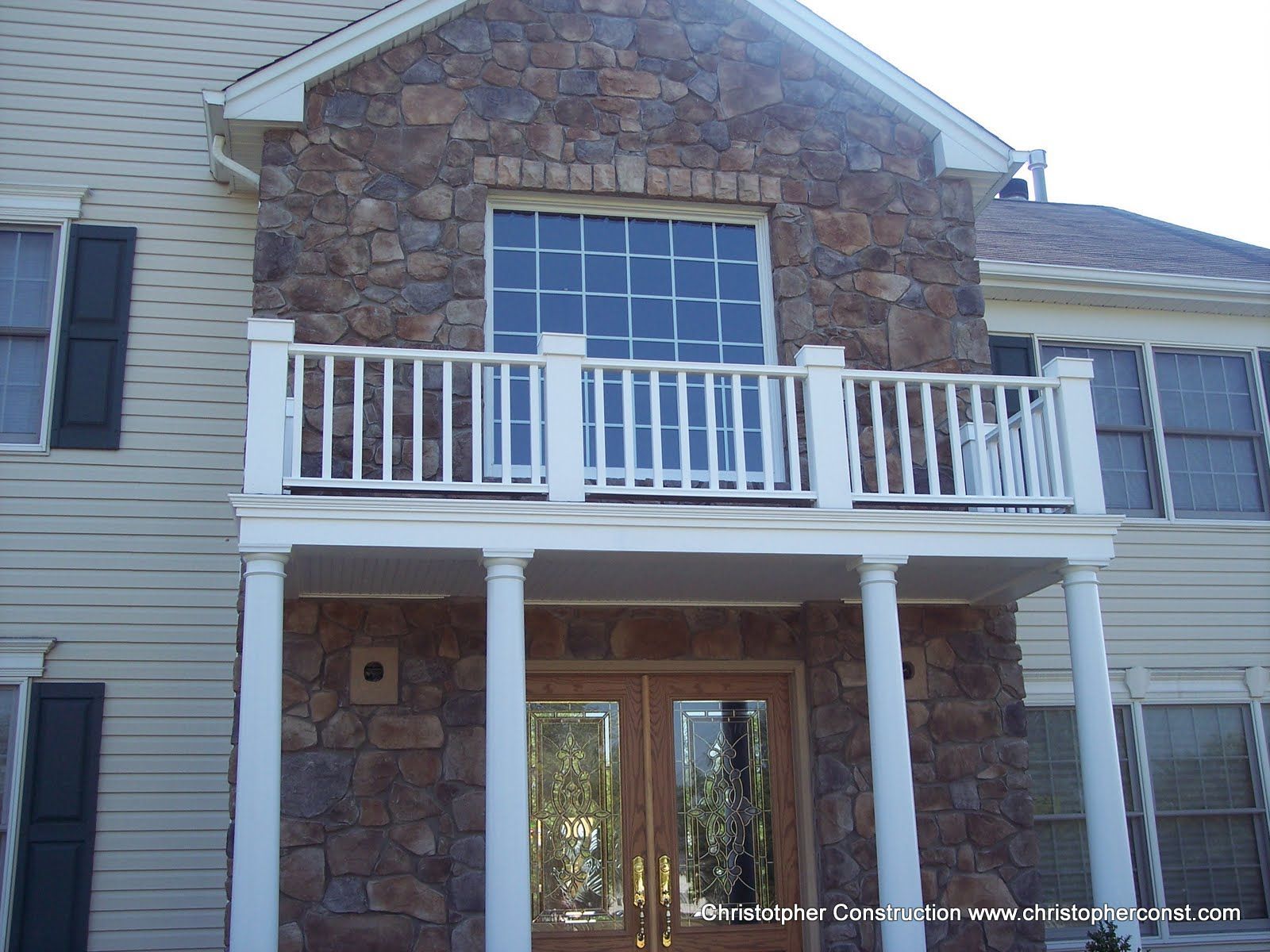 Stone-front house with white balcony and columns above a covered front porch