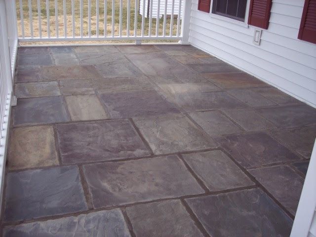 Stone patio beside a white house, with a railing and red shutters visible.