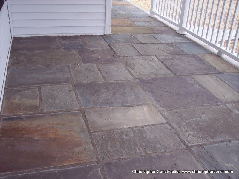 Stone patio with dark square pavers beside a house and white railing