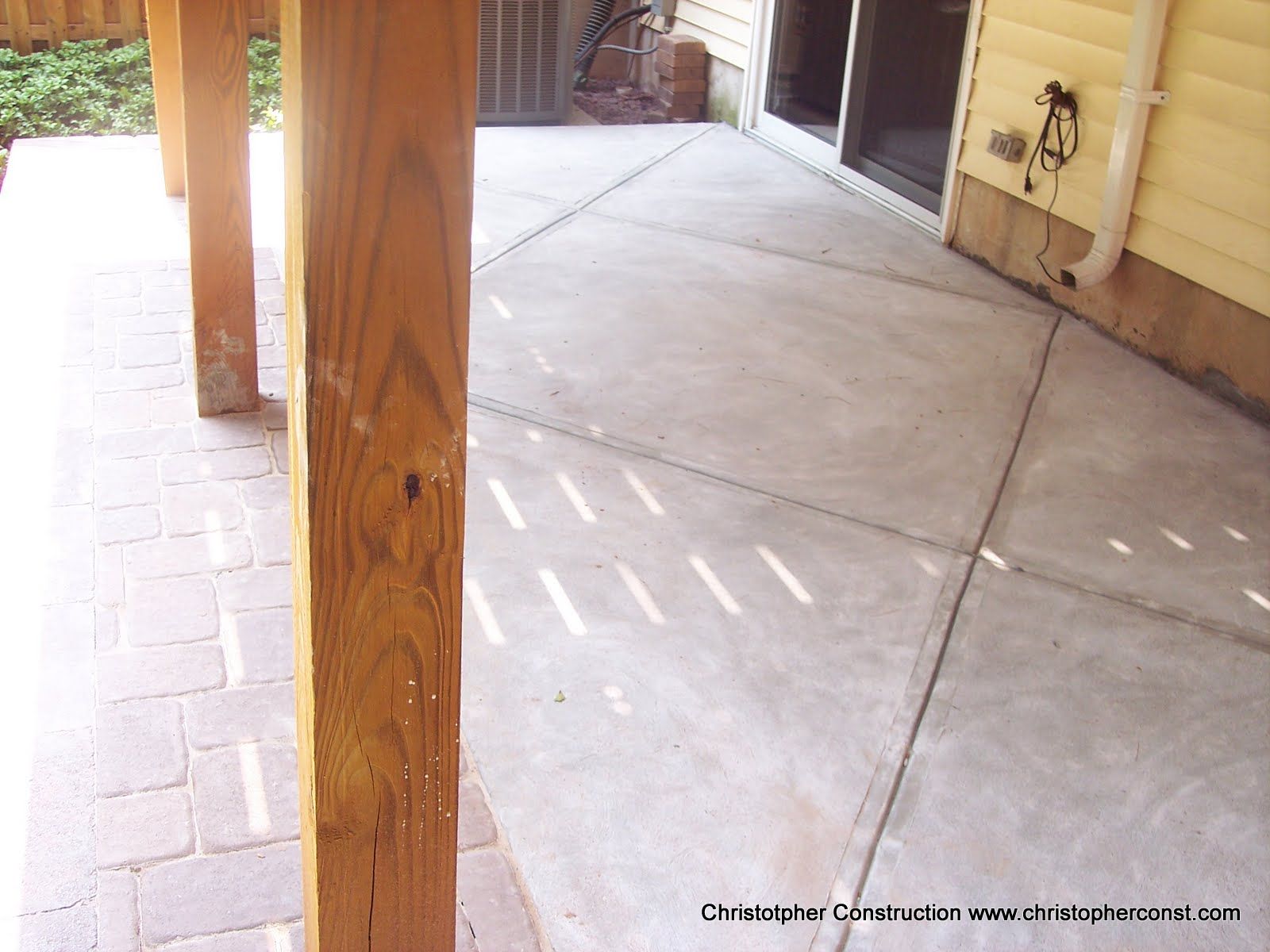 Covered concrete porch with wooden support posts and brick pavers on the left side.