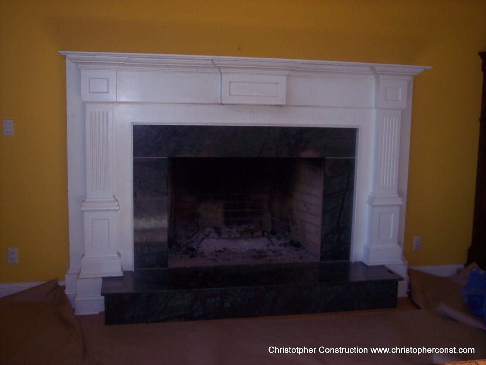 White fireplace mantel with black firebox against a yellow wall in a room