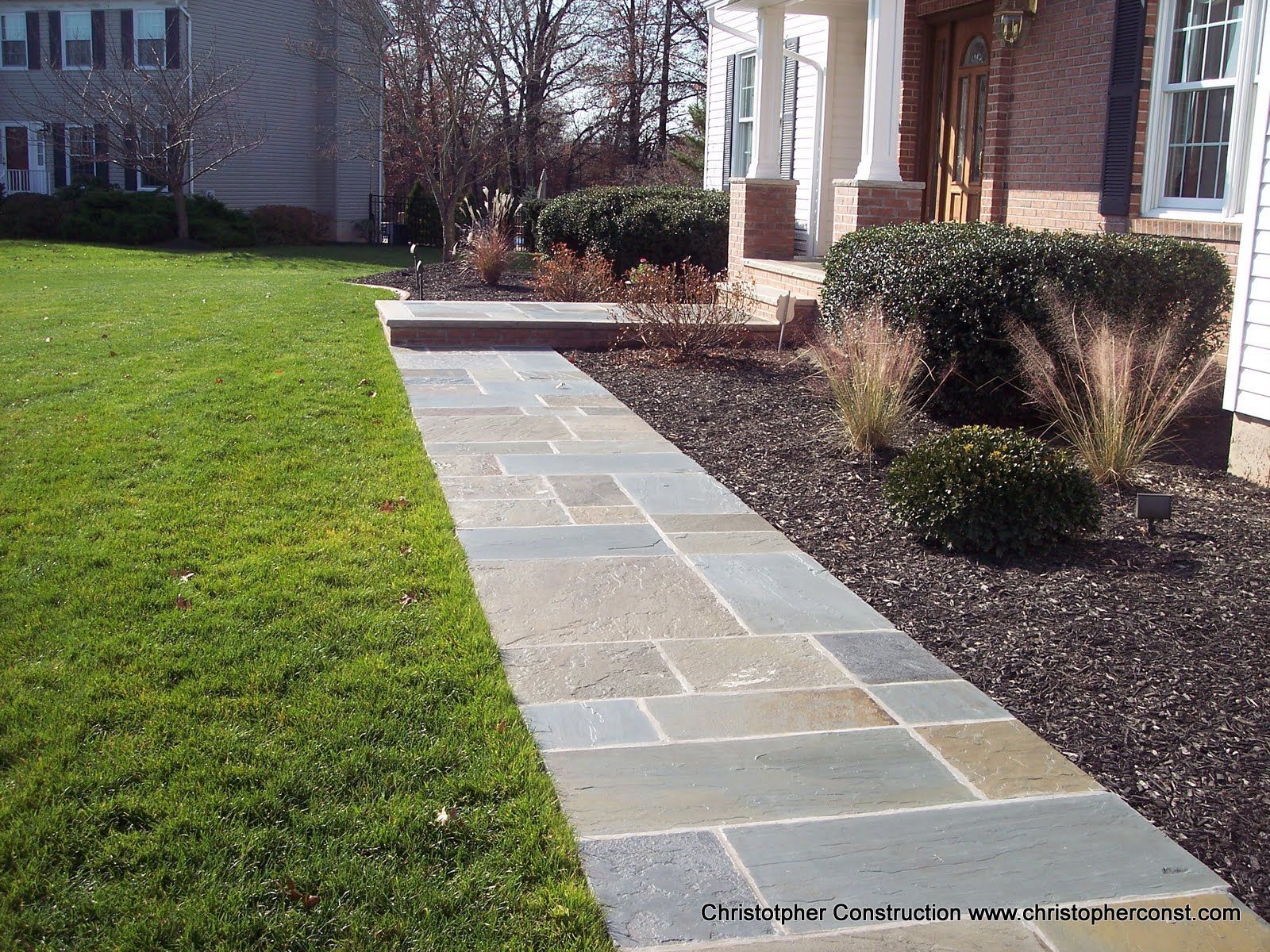 Stone walkway through green lawn beside a house and shrubs