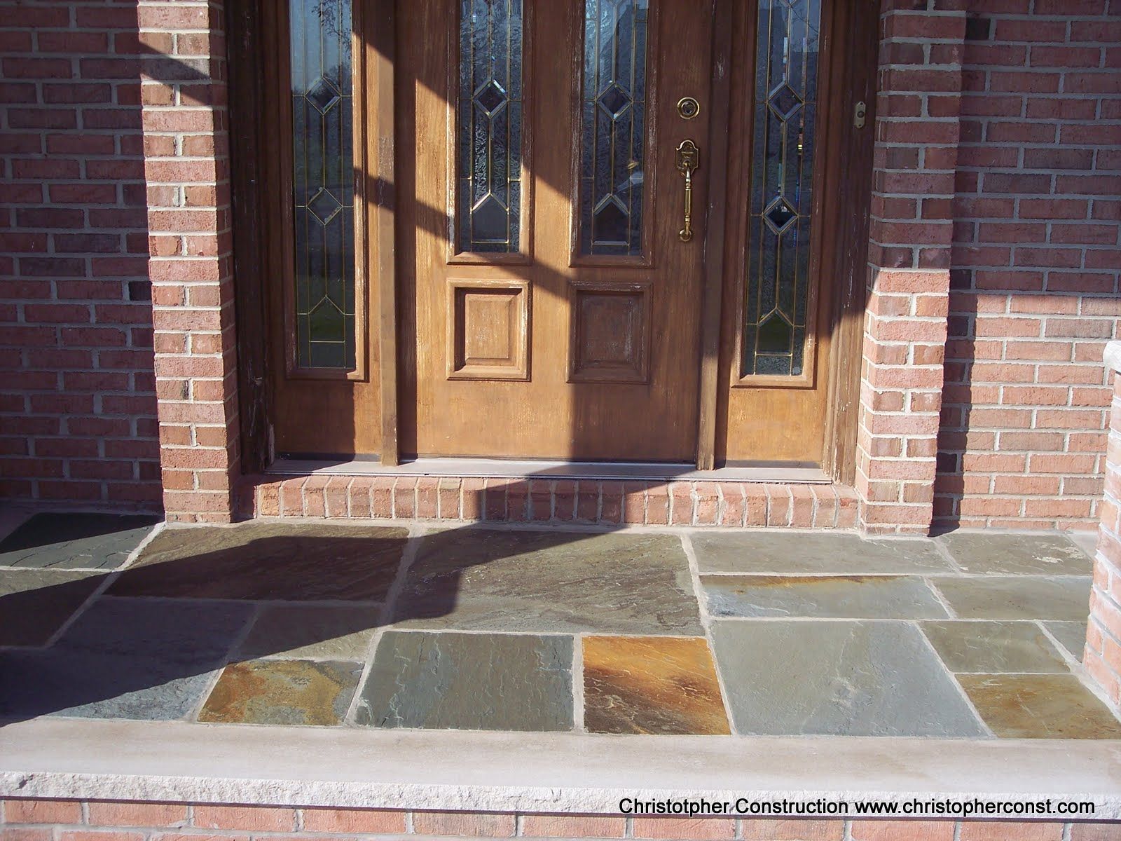 Brick front porch with wooden double doors and tiled steps in sunlight