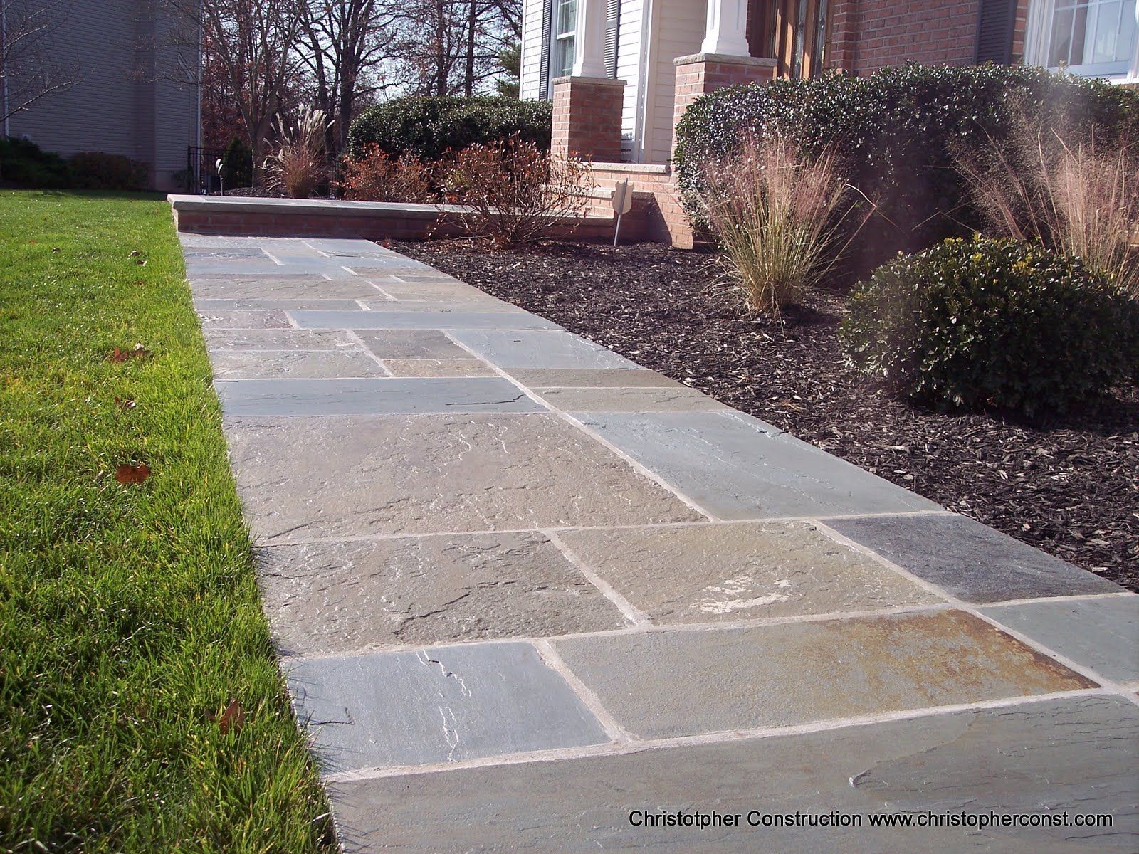 Stone walkway beside green lawn and trimmed shrubs in a sunny garden area