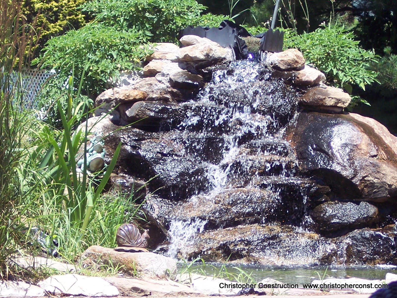 Small waterfall cascading over rocks in a lush garden with green plants around it