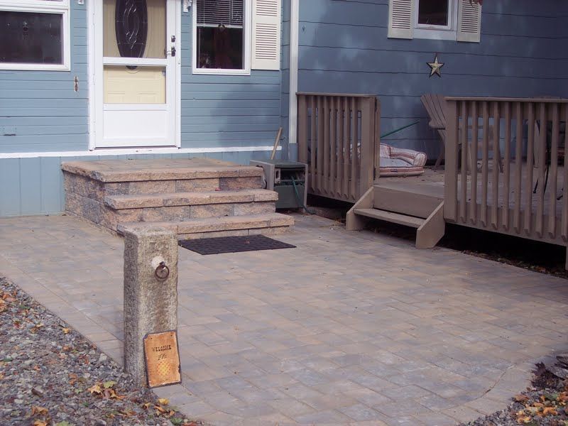 Patio with paver stones, wooden deck steps, and a small fire pit in front of a house