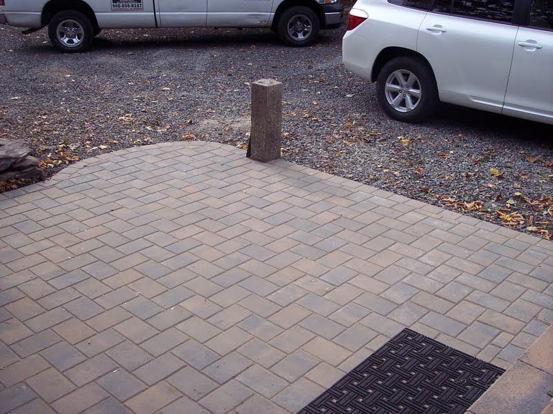 Brick-paved parking area with a short post, parked cars, and a gravel surface nearby