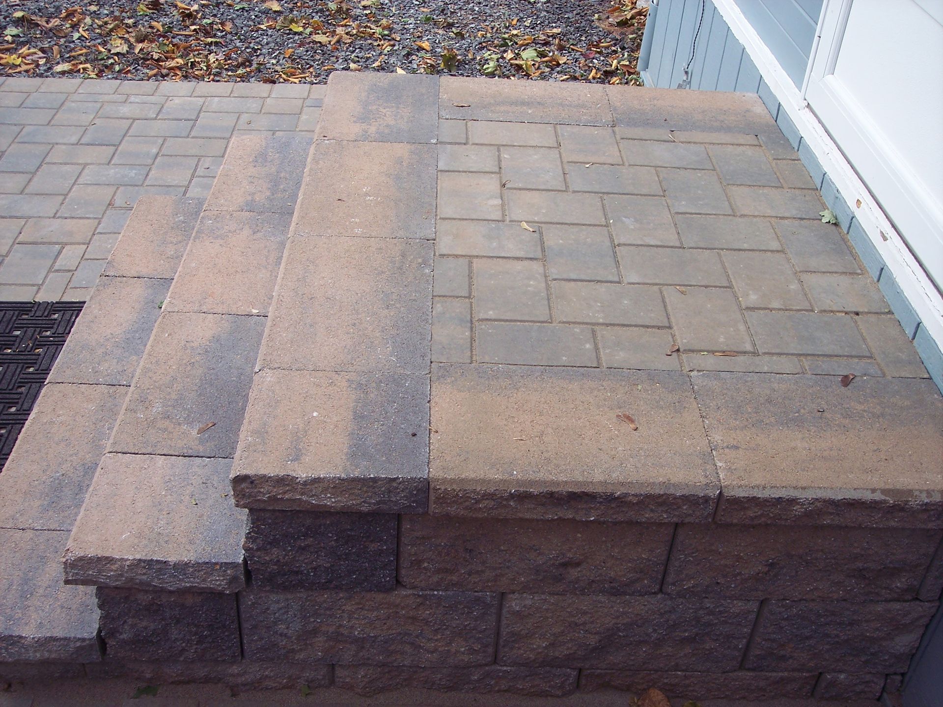 Stone patio with raised step and dark gravel border beside a building
