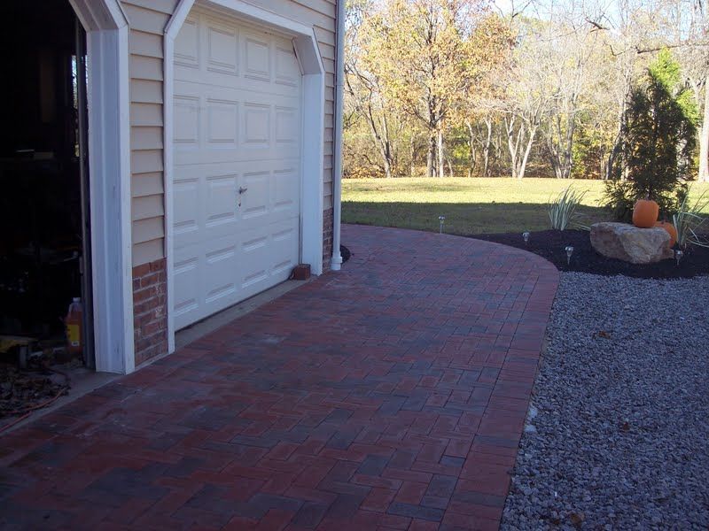 Brick walkway beside a white garage, curving toward a gravel yard with a pumpkin decoration.