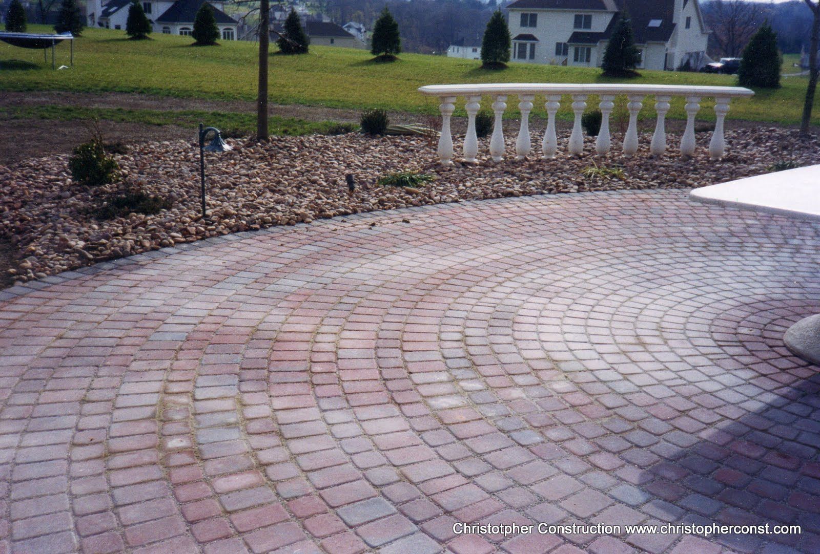 Curved brick patio beside a white railing in a landscaped yard