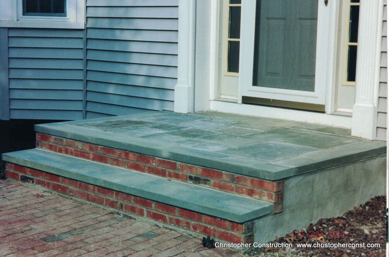 Front porch with green-painted steps and brick risers on a blue house