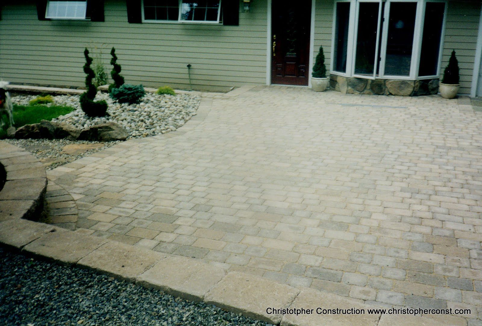 Paved brick walkway leading to a house entrance with landscaping and a front door