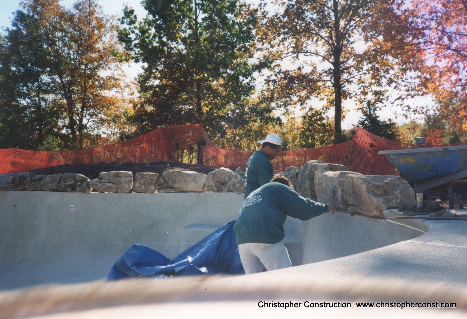 Person pulling a blue tarp over a concrete pool with autumn trees and rocks in the background