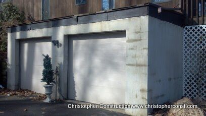Small gray garage or shed with white doors beside a lattice fence, in dappled sunlight.