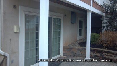 Covered patio with white columns, sliding glass doors, and a gravel yard beside a house