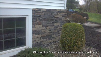 House exterior with white siding, stone veneer wall, and trimmed round shrub beside a window.