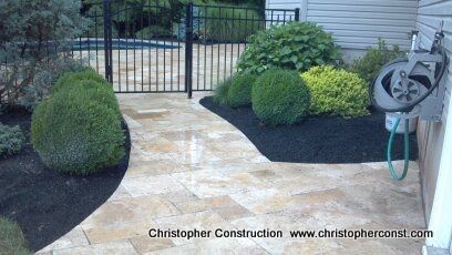 Stone walkway leads to black gate through landscaped yard with trimmed shrubs and dark mulch.