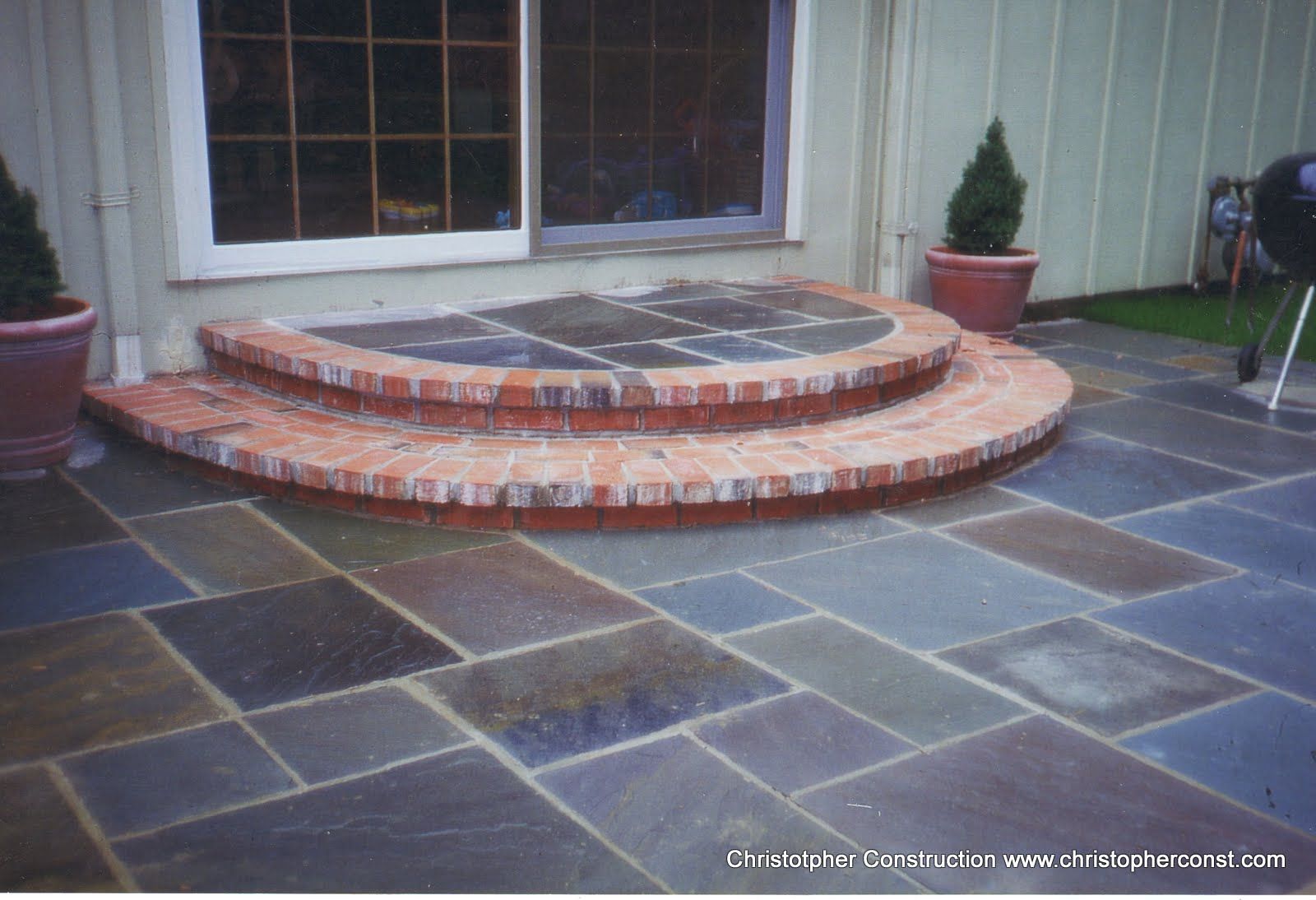 Curved brick steps leading to a small patio with slate pavers in front of a house