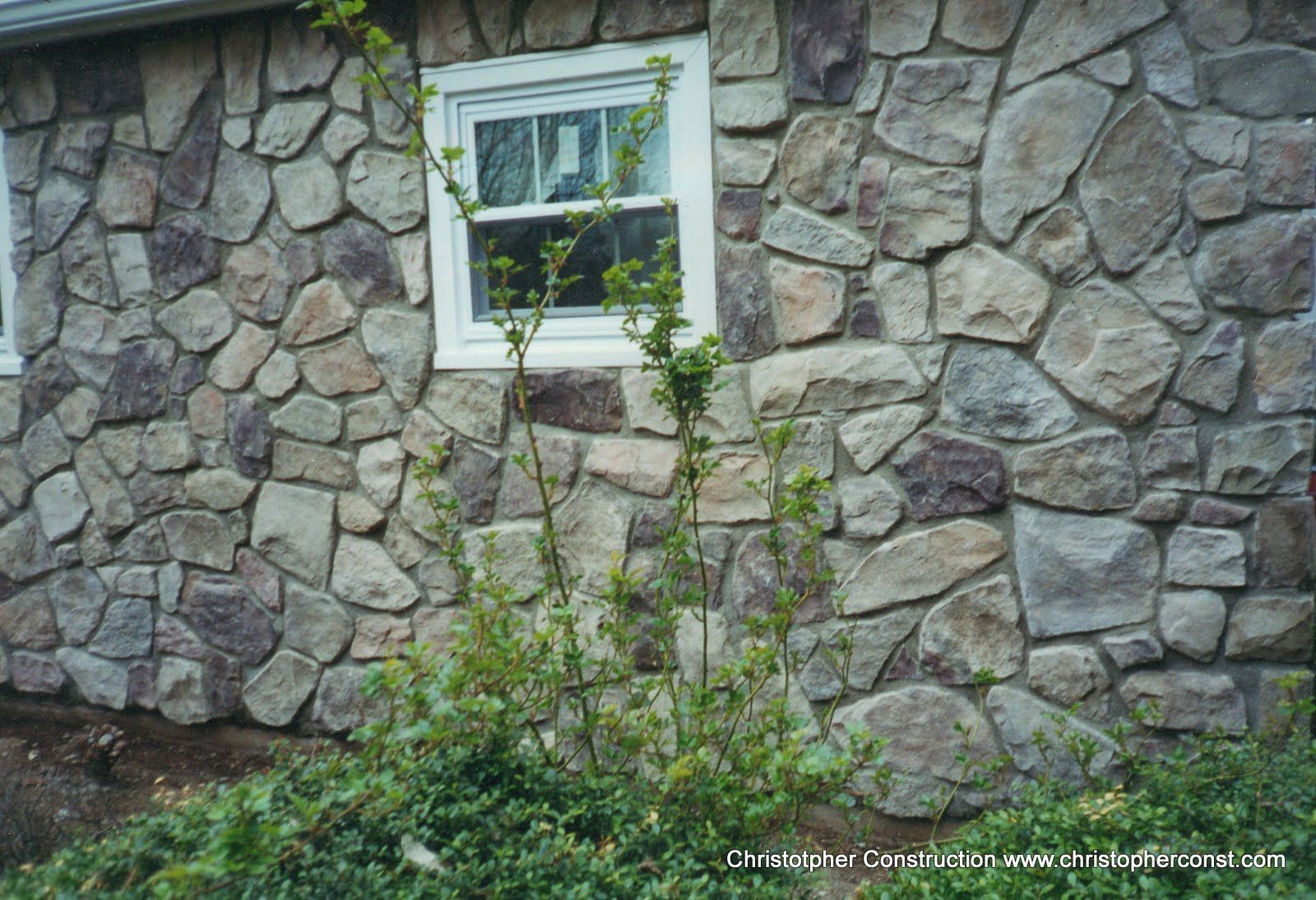 Stone wall with a small window, partly covered by green vines and plants.