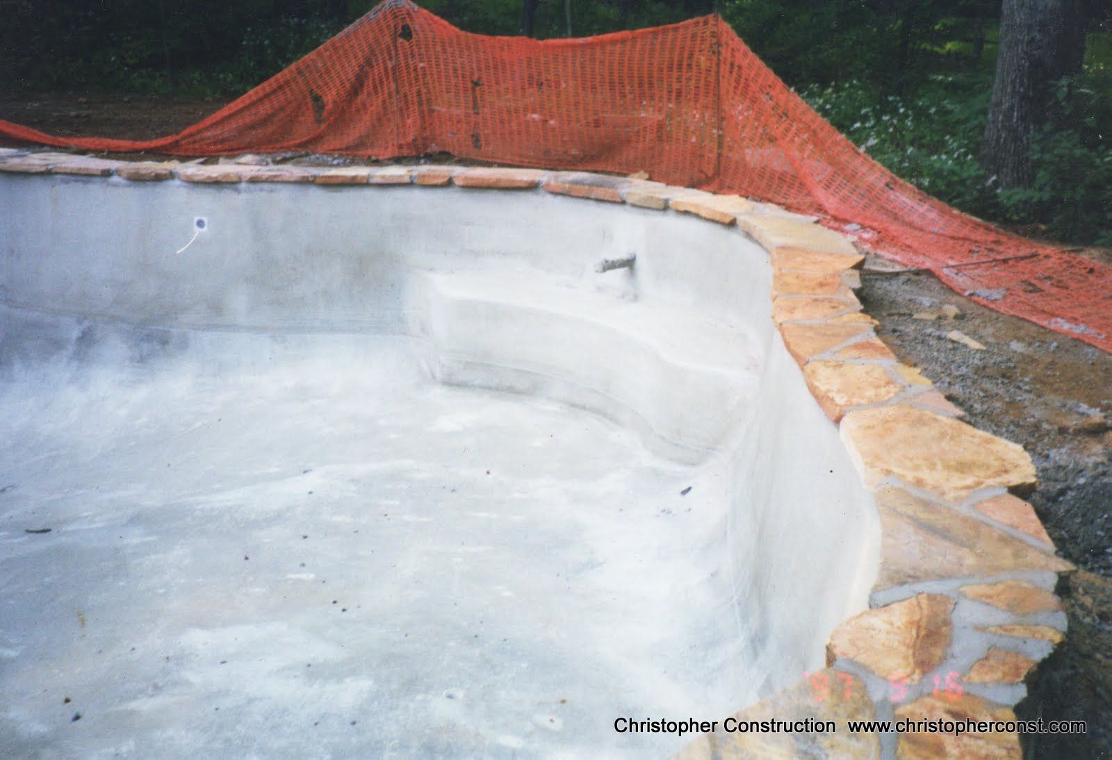 Empty concrete swimming pool under construction, with orange safety netting along the edge.