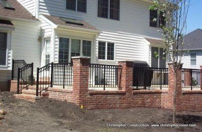 Brick patio with black metal railing and red brick columns beside a white house