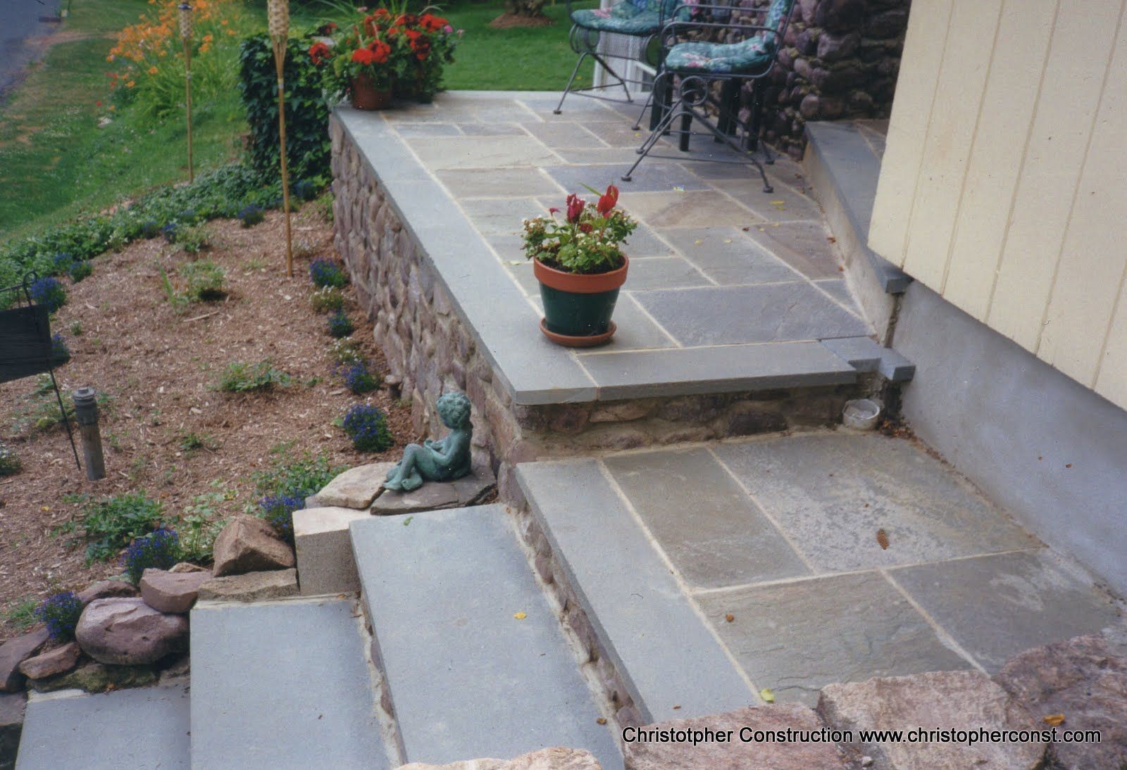 Stone patio steps beside a house with potted plants and a small garden bed