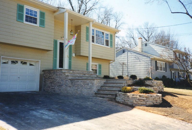 Suburban house with garage, front steps, flag, and landscaped yard on a sunny day