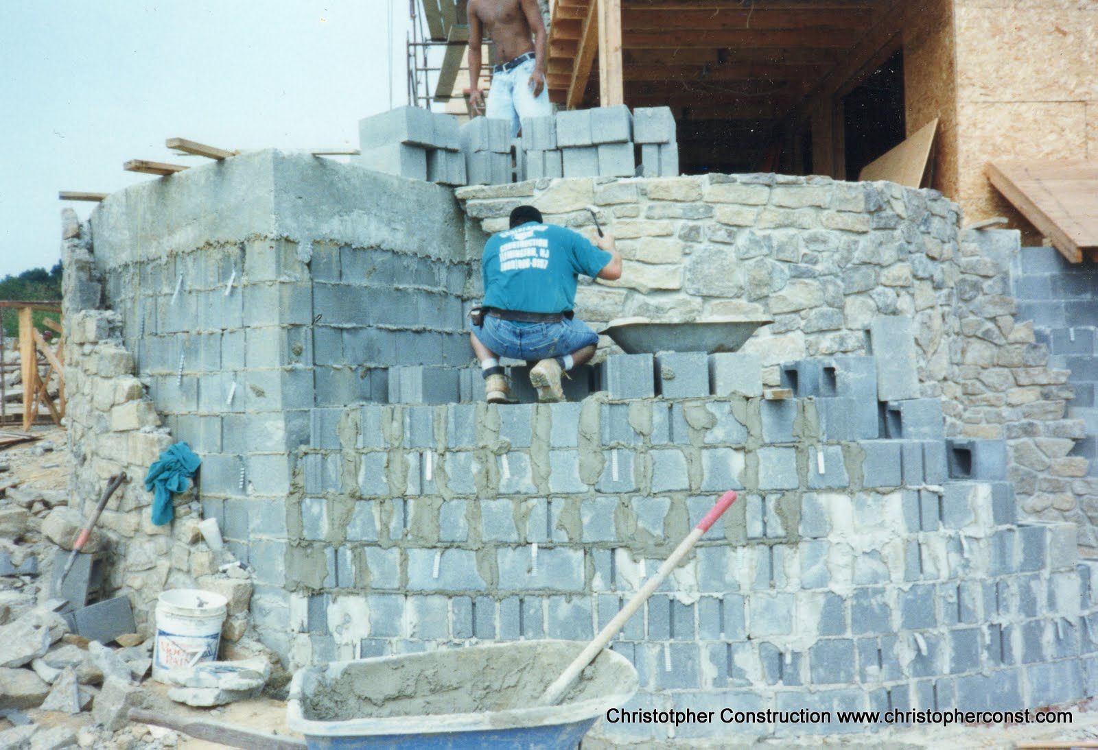 Worker stacking gray cinder blocks into a wall at a construction site