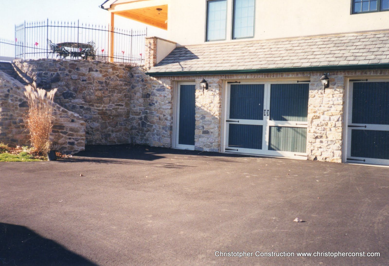 Exterior of a stone building with a paved driveway, double glass doors, and an upper balcony.