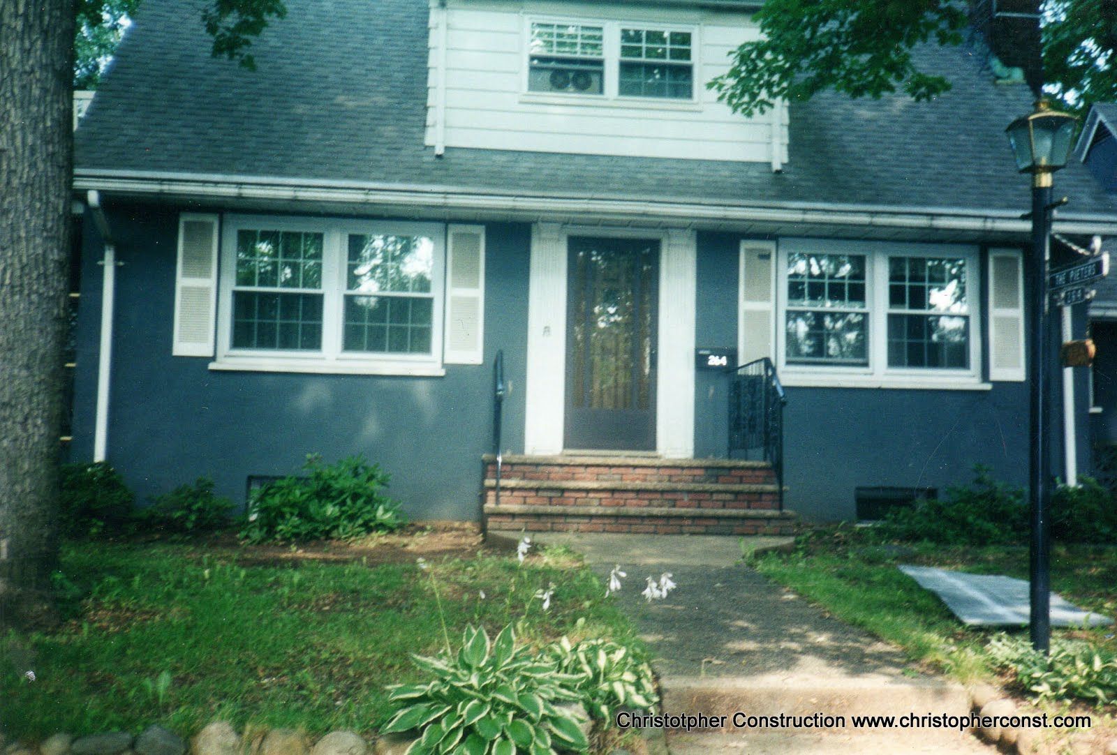 Front view of a gray two-story house with white trim, brick steps, and a small front yard.