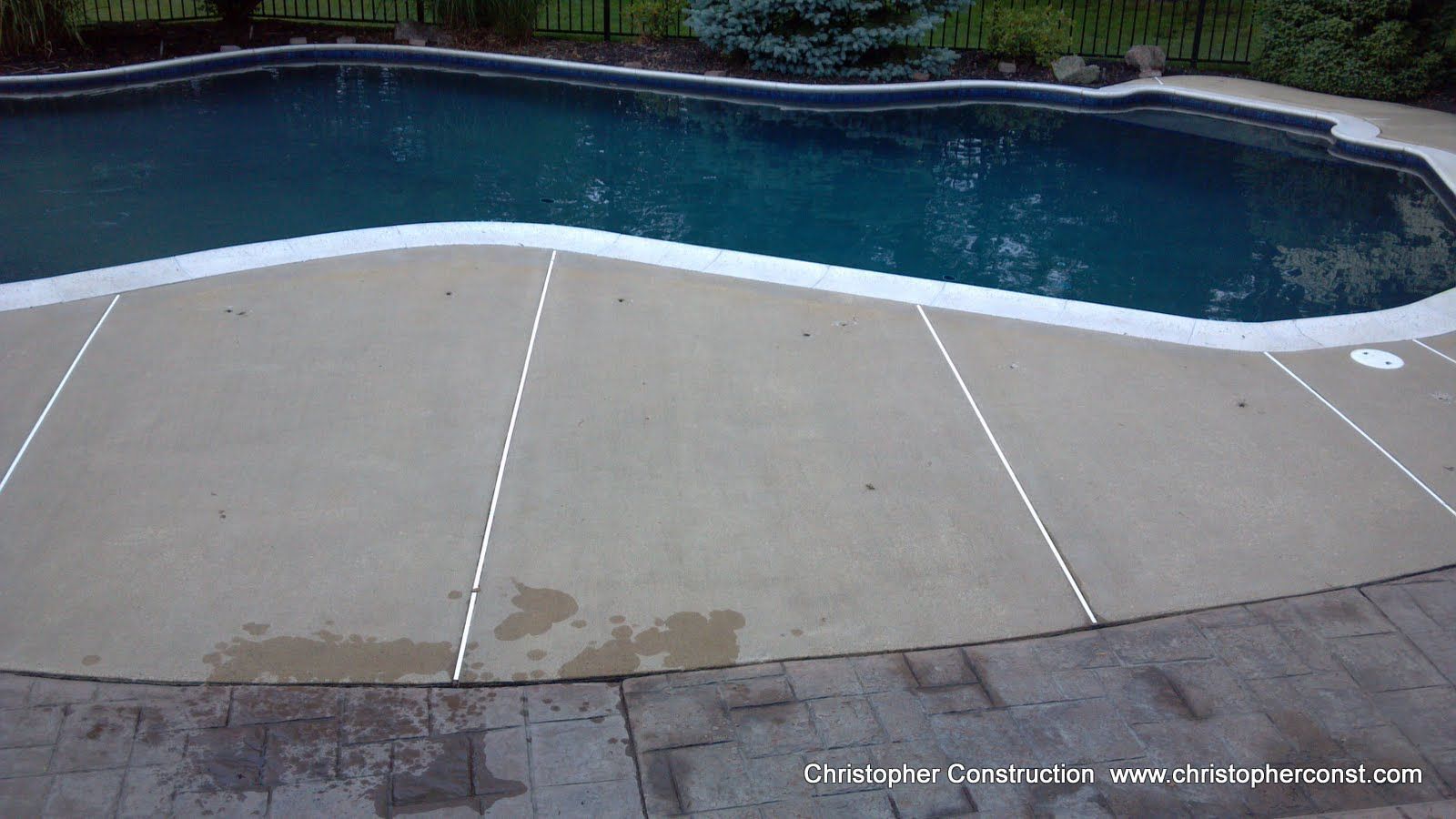 Empty backyard pool deck with water stains beside a dark blue swimming pool.