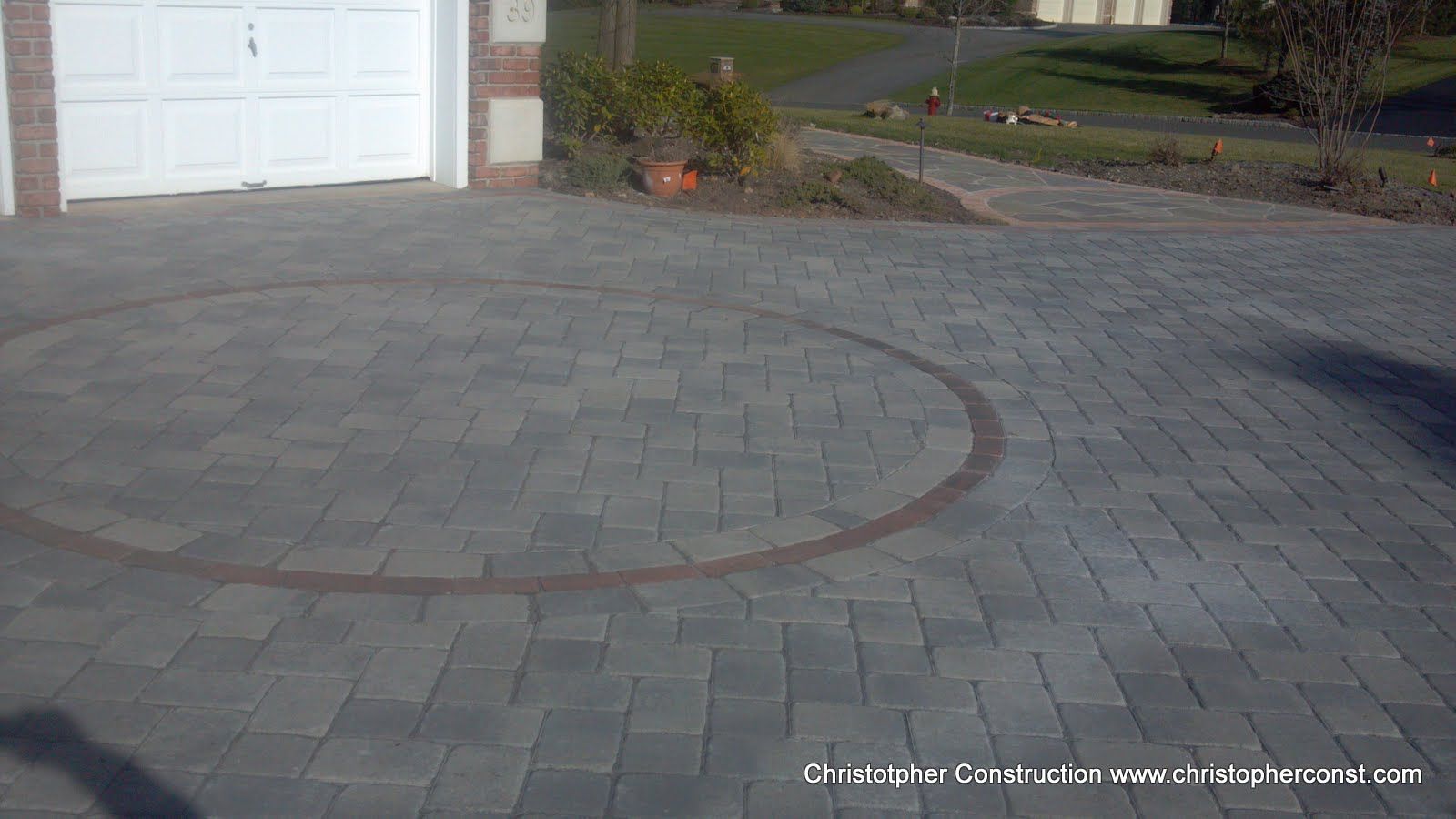 Paved driveway with a curved brick border leading to a white garage door and street beyond