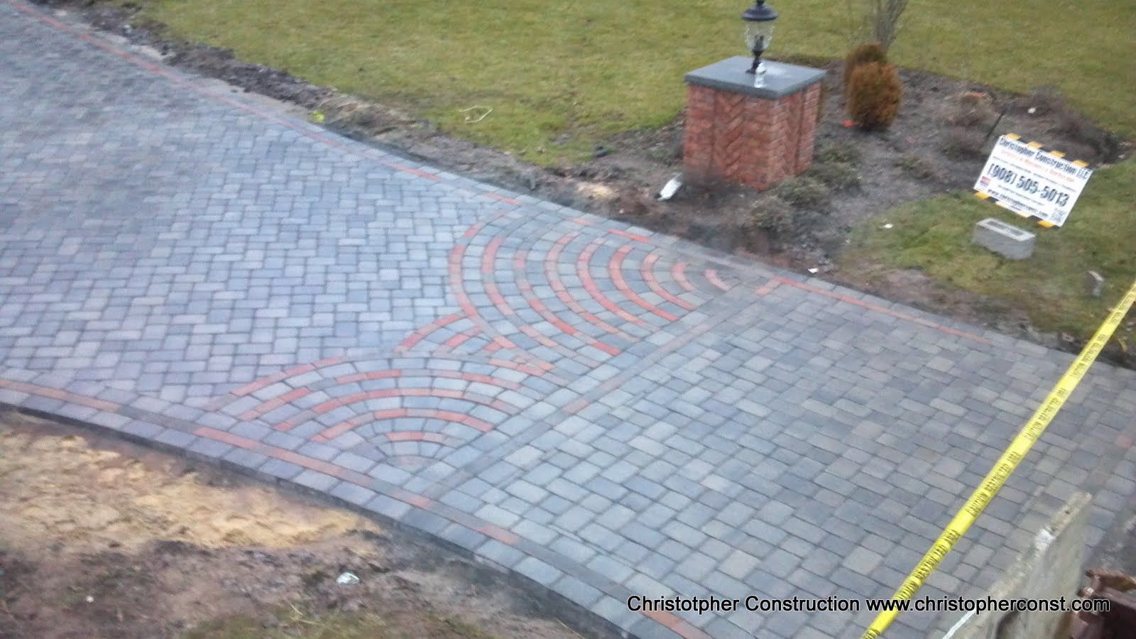Curved cobblestone driveway with a red tactile guidance strip leading to a lamp post and sign.