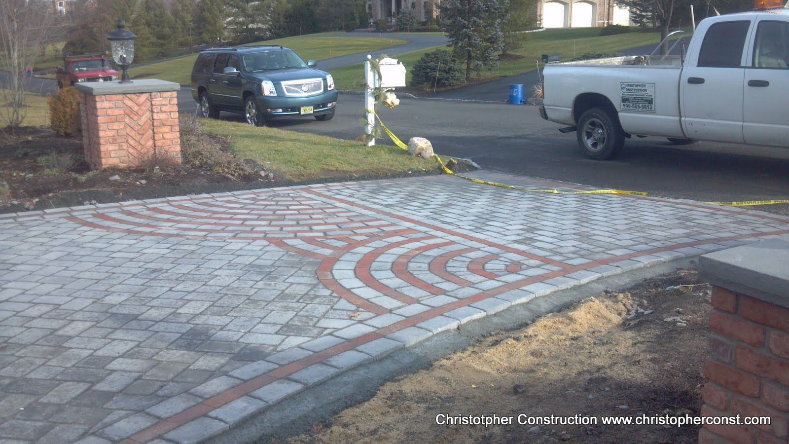 Paved driveway with circular inlaid brick design, parked cars, and a brick wall at the edge
