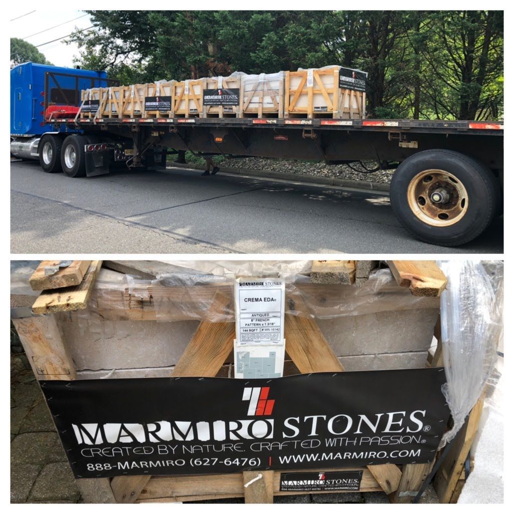 Flatbed trailer loaded with wrapped stone pallets, branded Marmo Stons, parked outdoors.