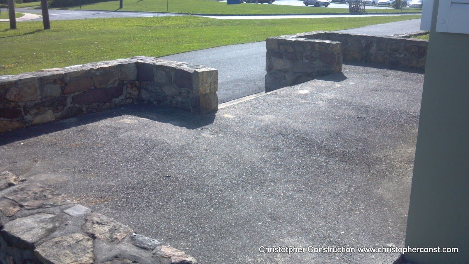 Stone patio with low walls beside a grassy lawn in bright sunlight