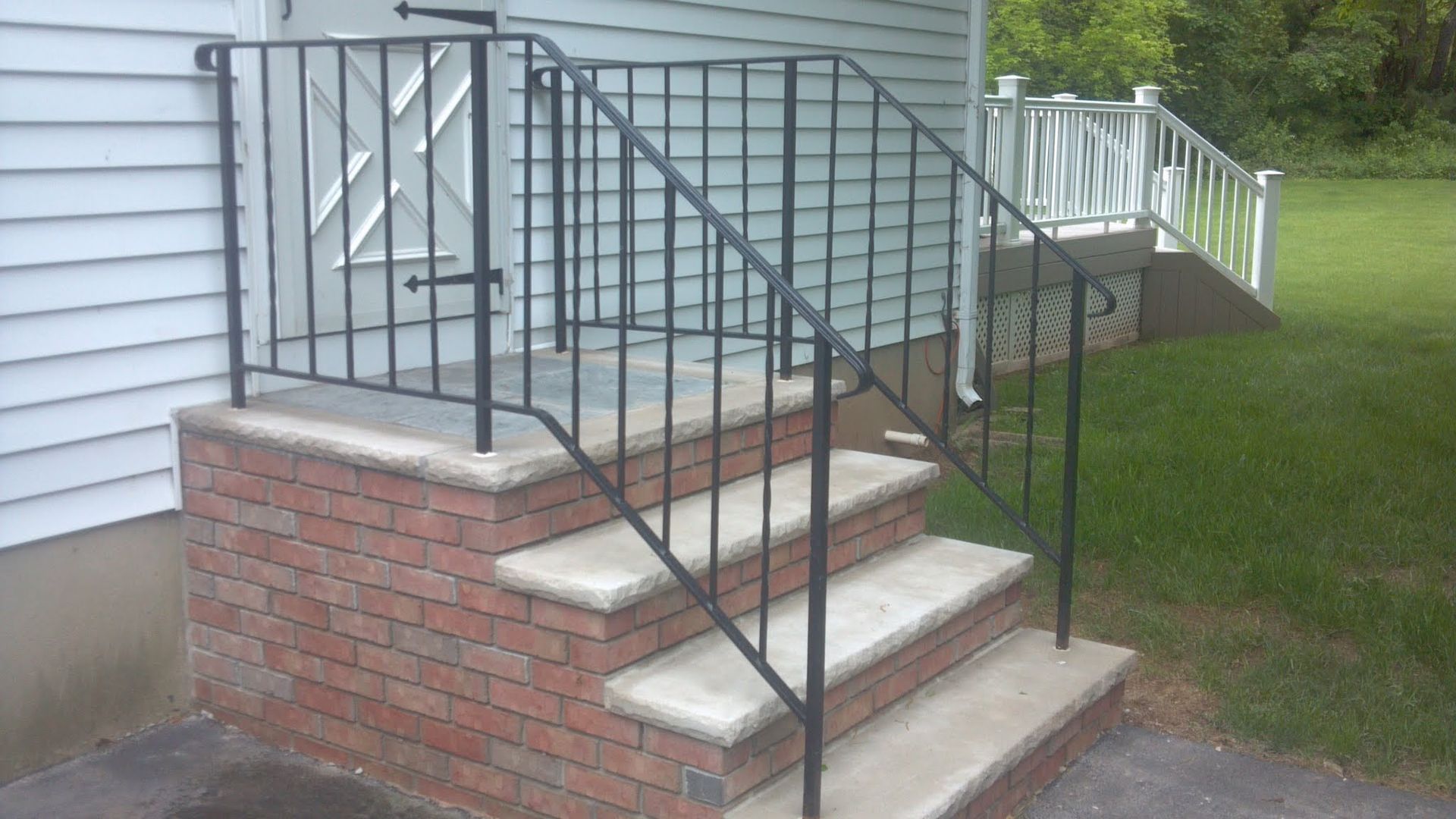 Brick front steps with black metal railings leading to a house porch and grassy yard