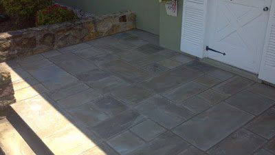 Stone patio with gray pavers beside a white door and retaining wall, lit by sunlight