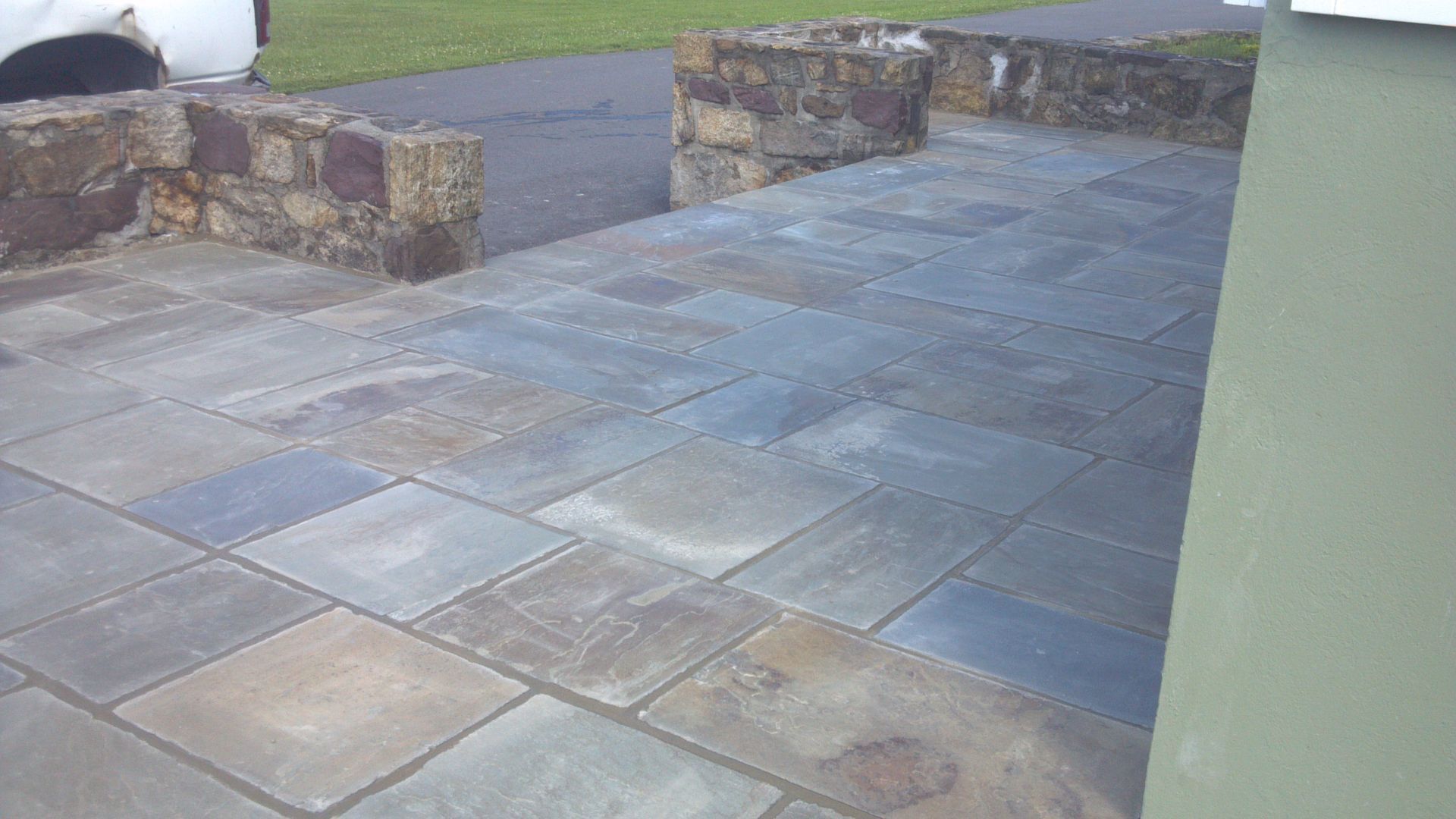 Stone patio with blue-gray paving and low stone walls beside a grassy lawn
