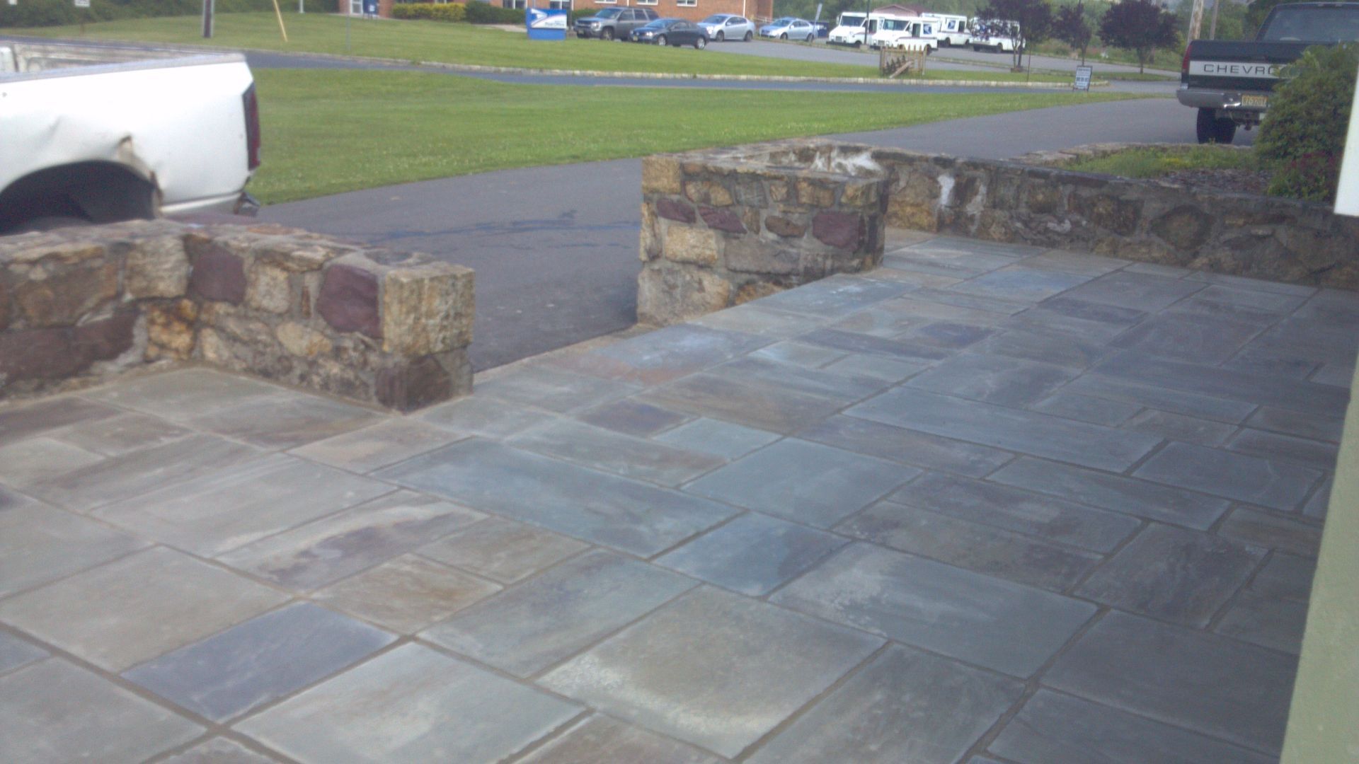 Stone patio with low brick walls beside a grassy roadside area
