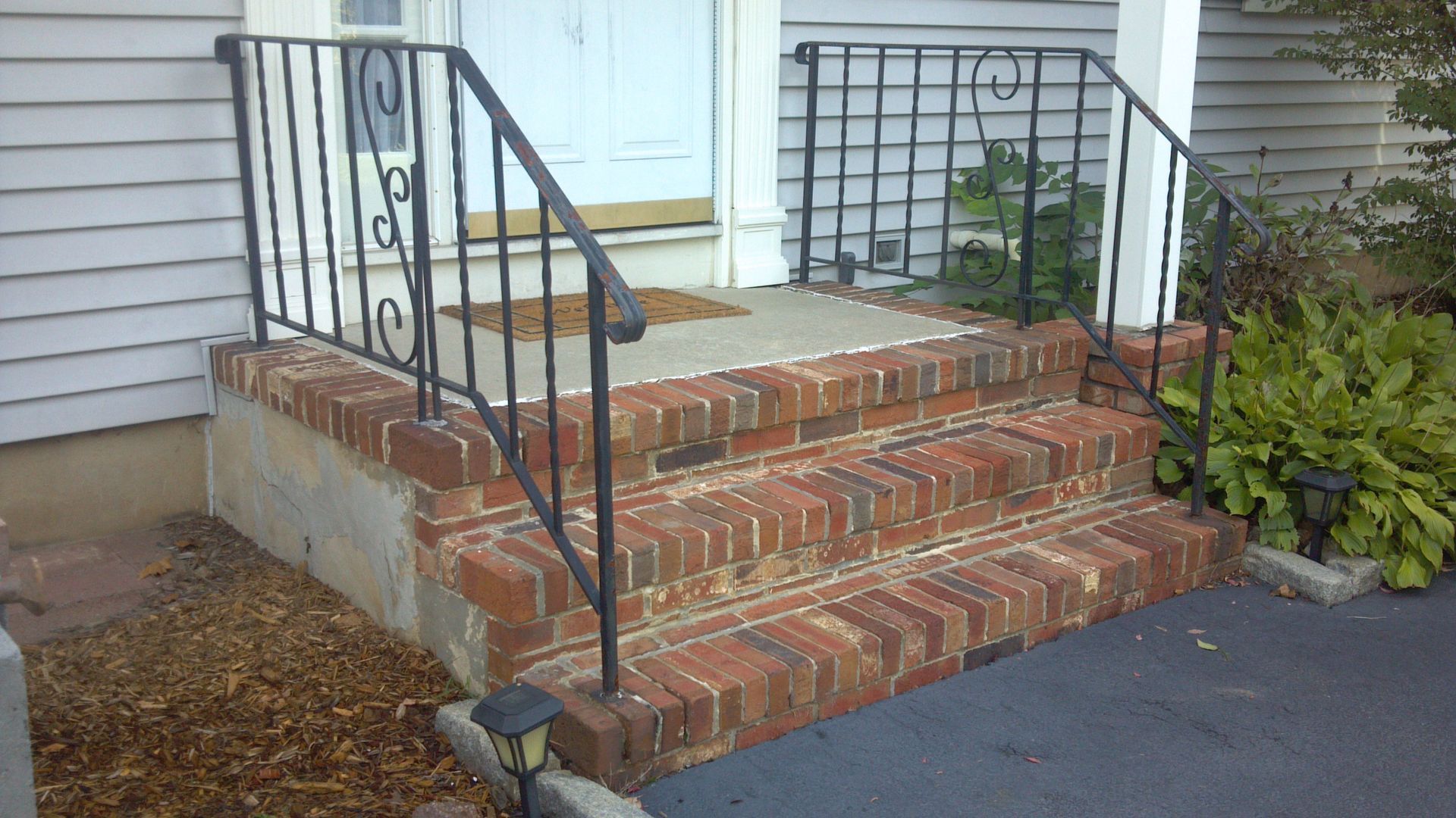 Brick front steps with black railings leading to a white house entryway