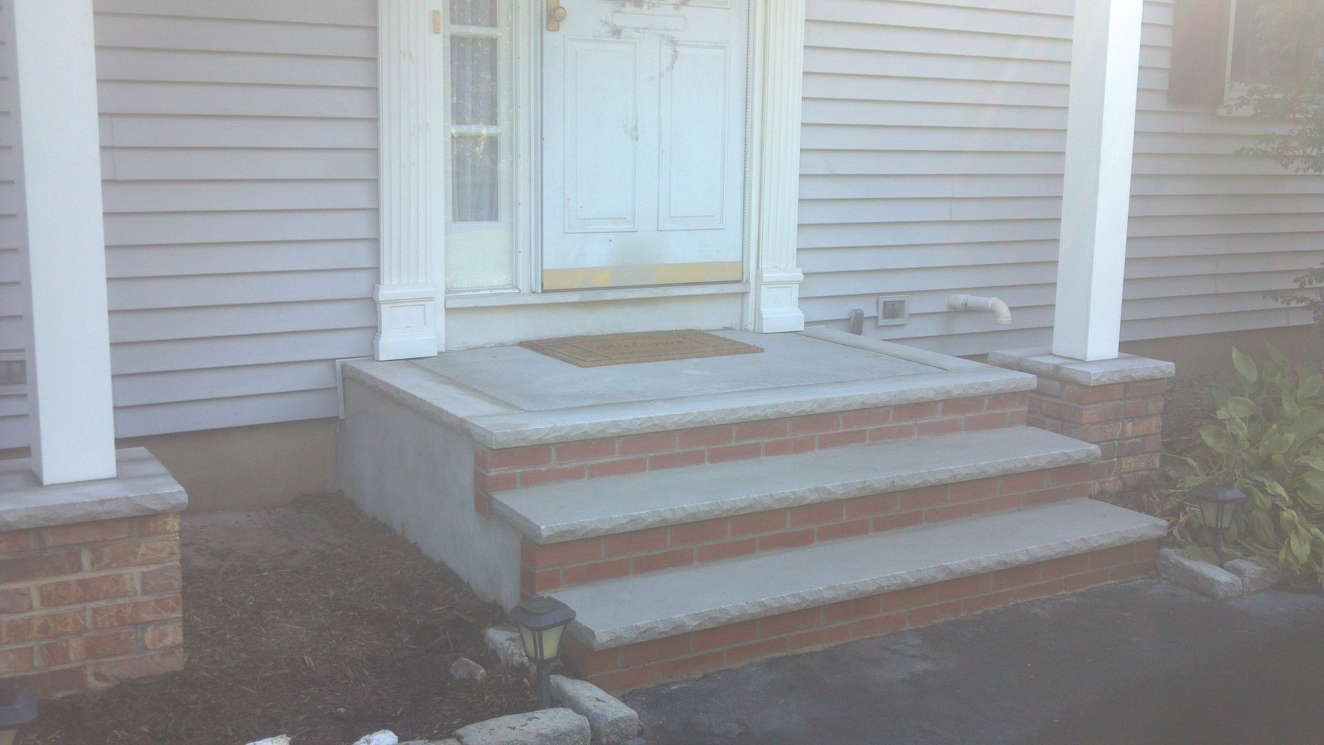 Front steps with white railings leading to a white front door on a gray house.