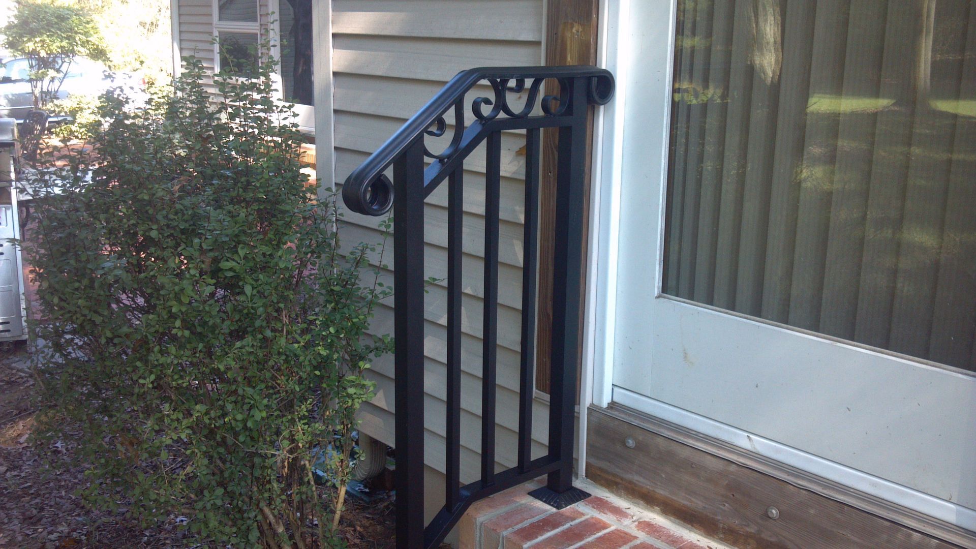 Black metal porch railing beside a brick step and white sliding glass door