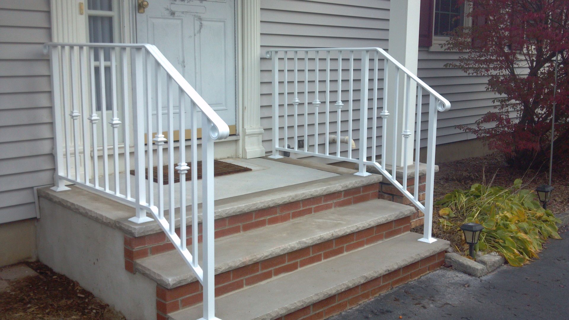 Front porch with brick steps, white railings, and a small landing beside a house.