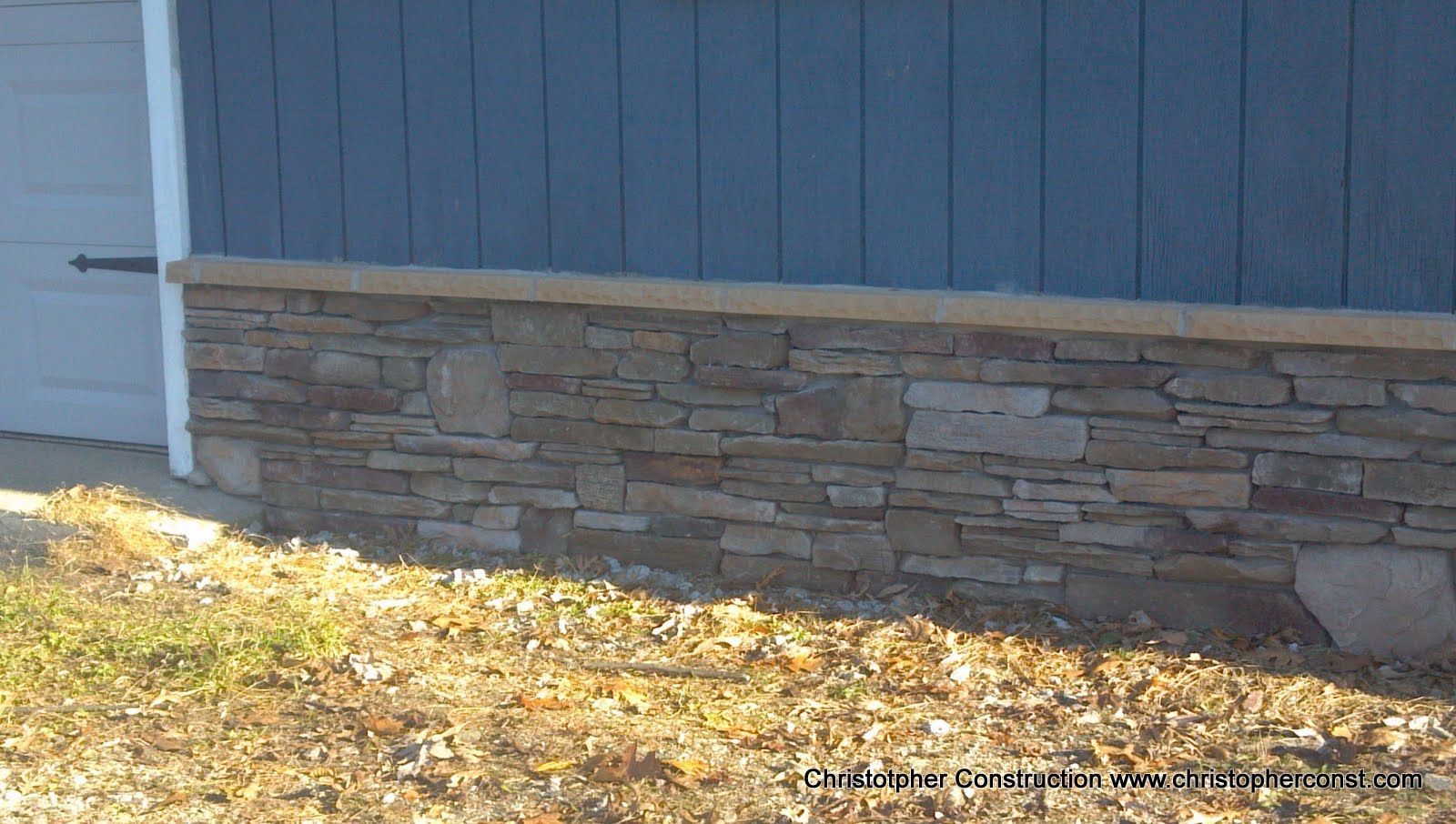 Blue building wall above a stone foundation with dry leaves along the ground