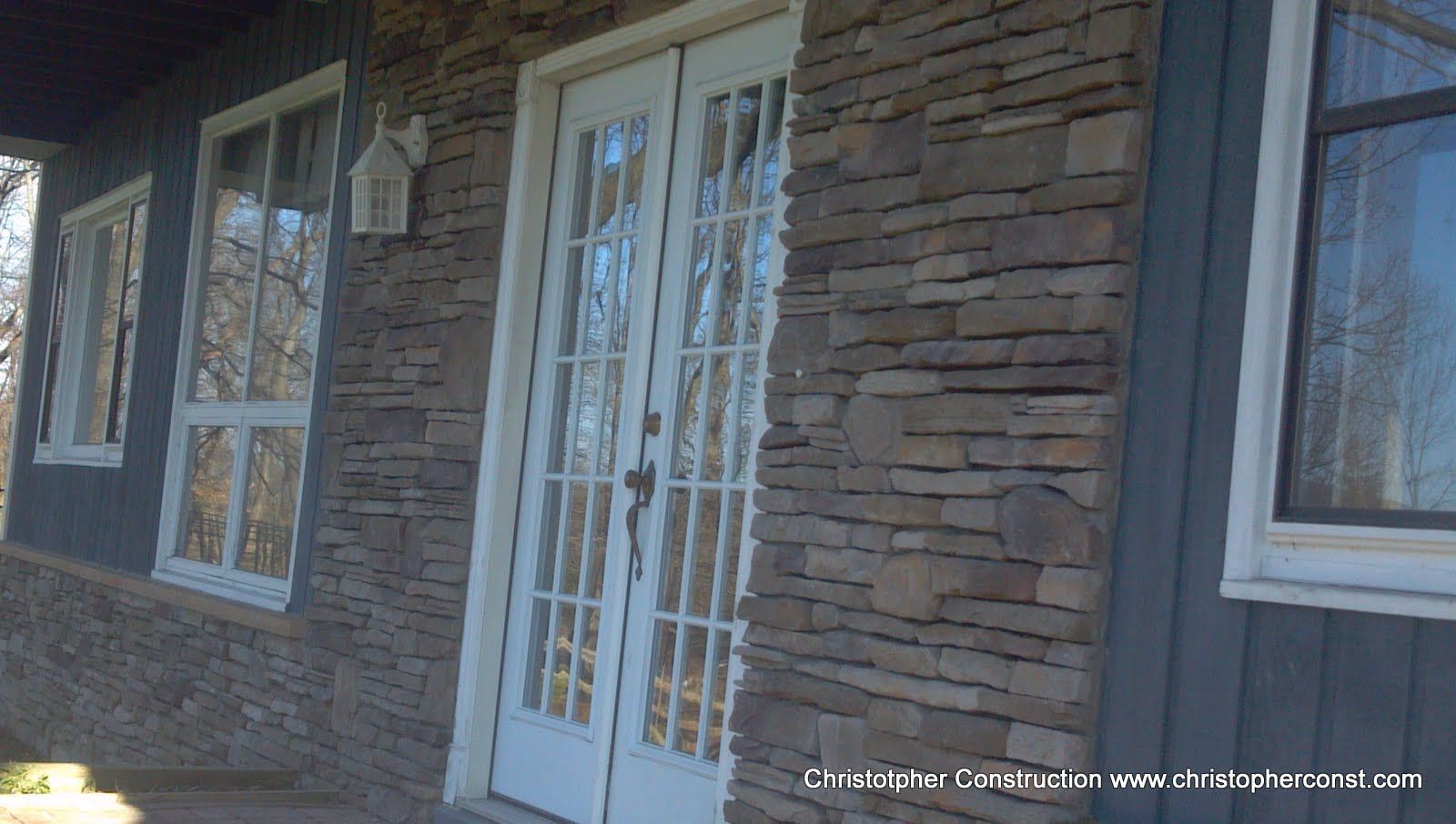 Stone house entrance with white double doors and windows, viewed from a covered porch