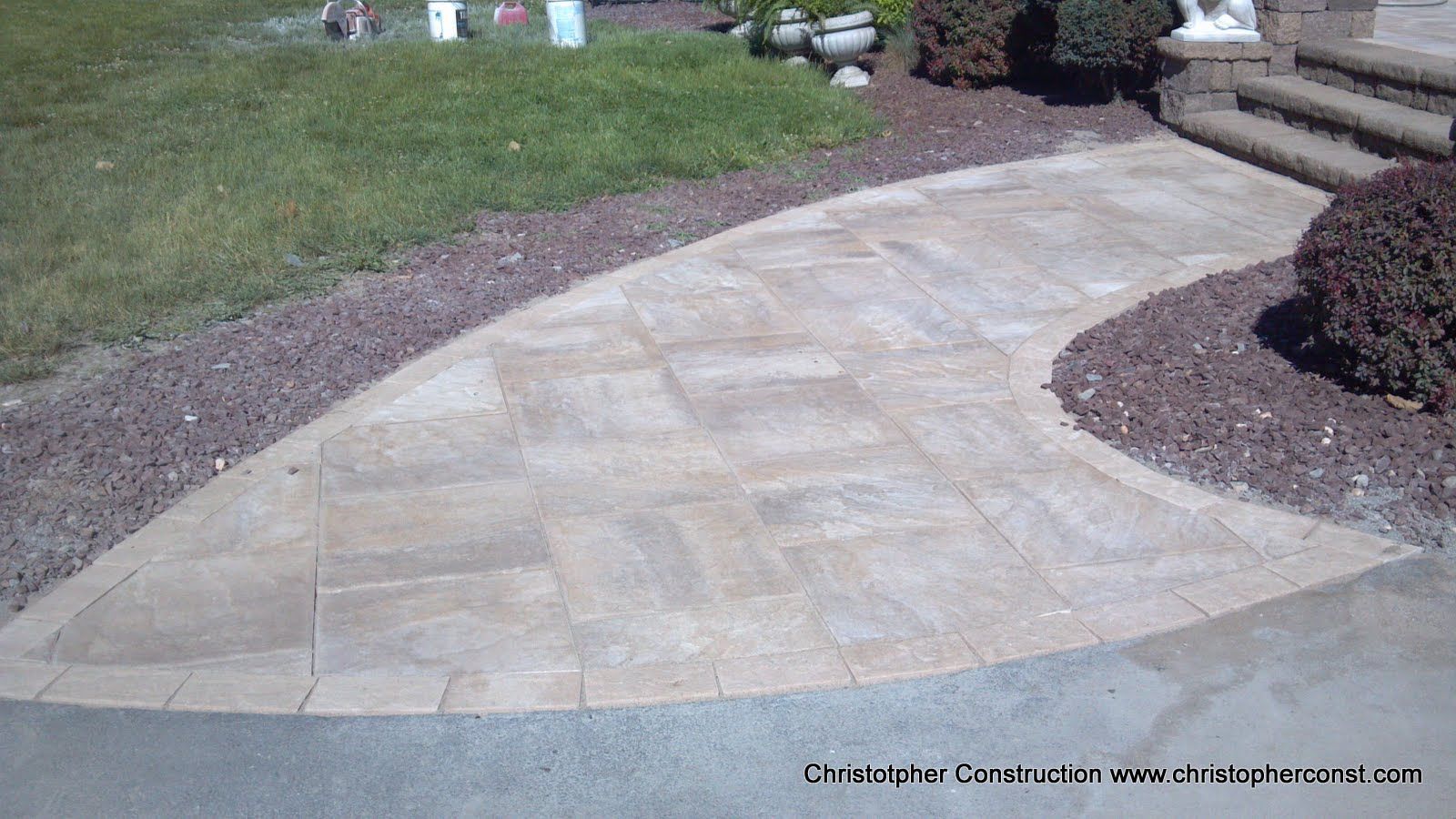 Curved stone walkway through a landscaped yard with grass, mulch, and shrubs